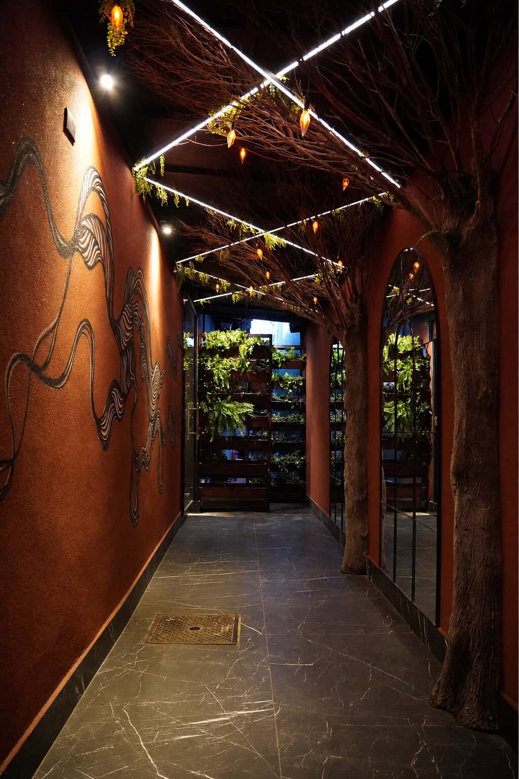 Corredor de entrada com desenhos na parede de terracota, espelhos em arco e folhagens no teto.