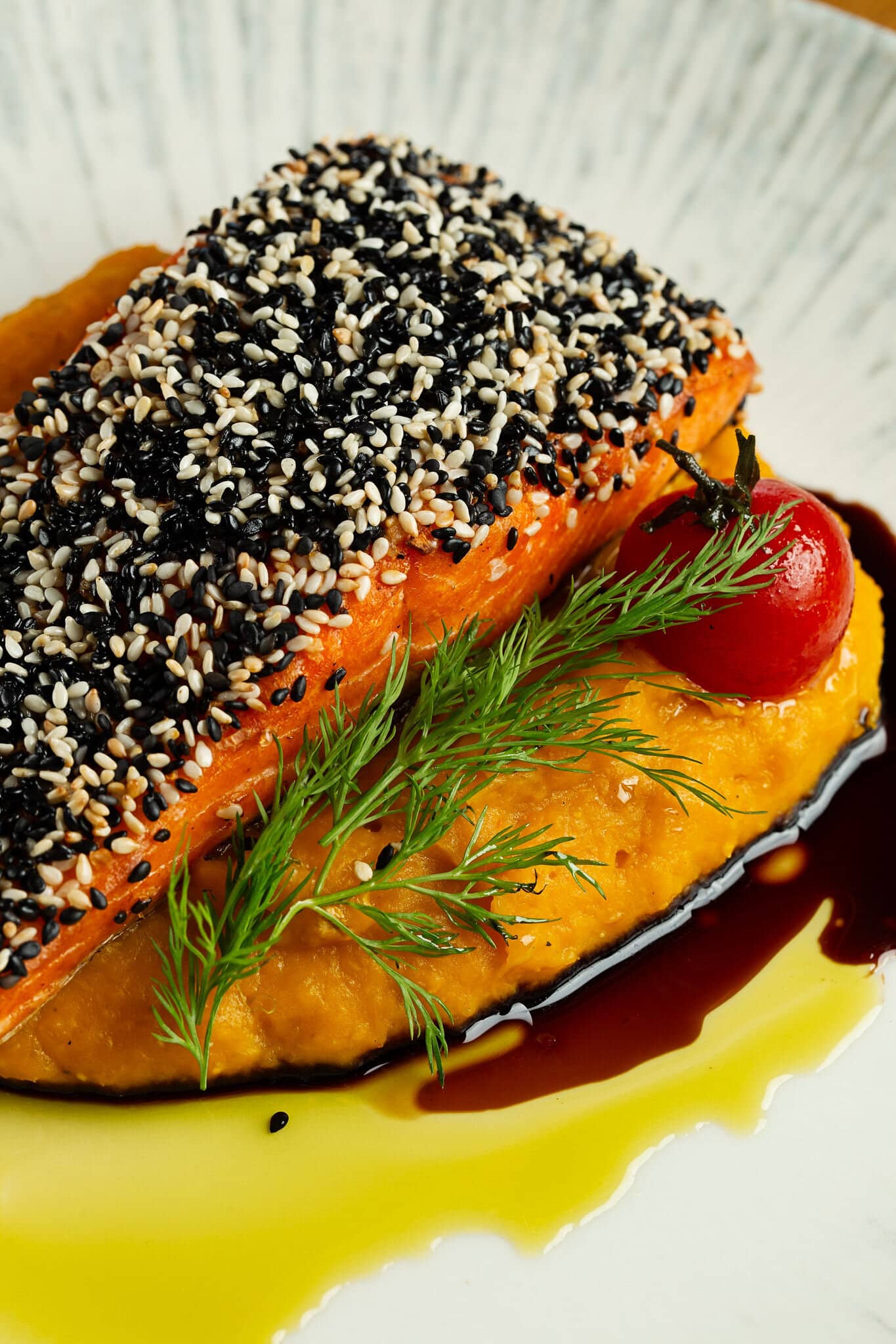 Filé de salmão com crosta de gergelim preto e branco sobre purê alaranjado, com azeite e tomate-cereja.